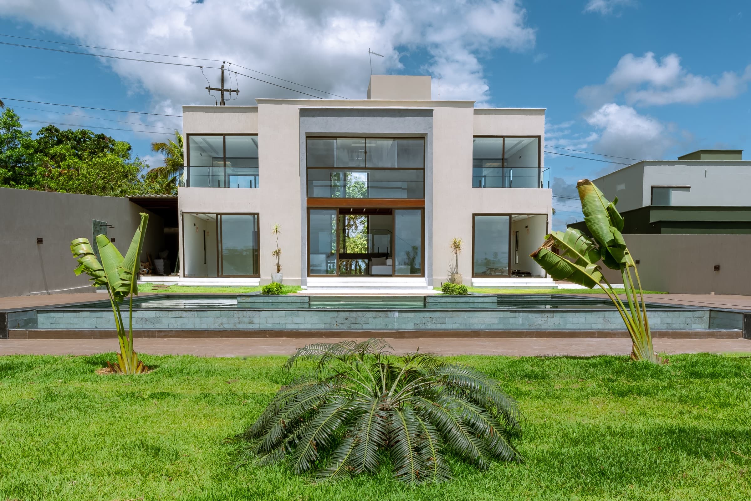 Fachada frontal da Luxo Oásis, com espelho d'água refletindo a casa